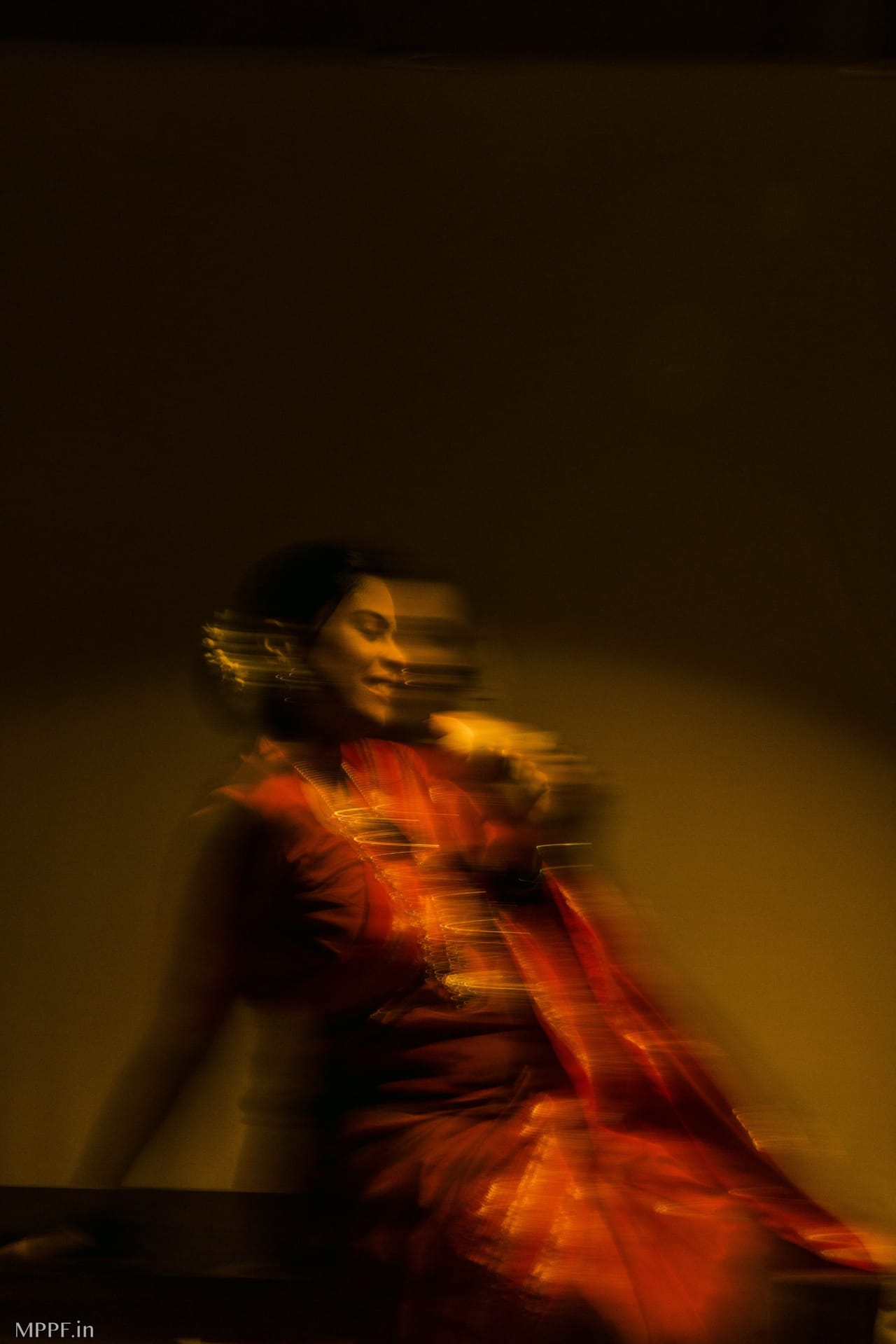 A long exposure of a woman in a red saree in warm light, her movement turning her jewellery into trails of gold.